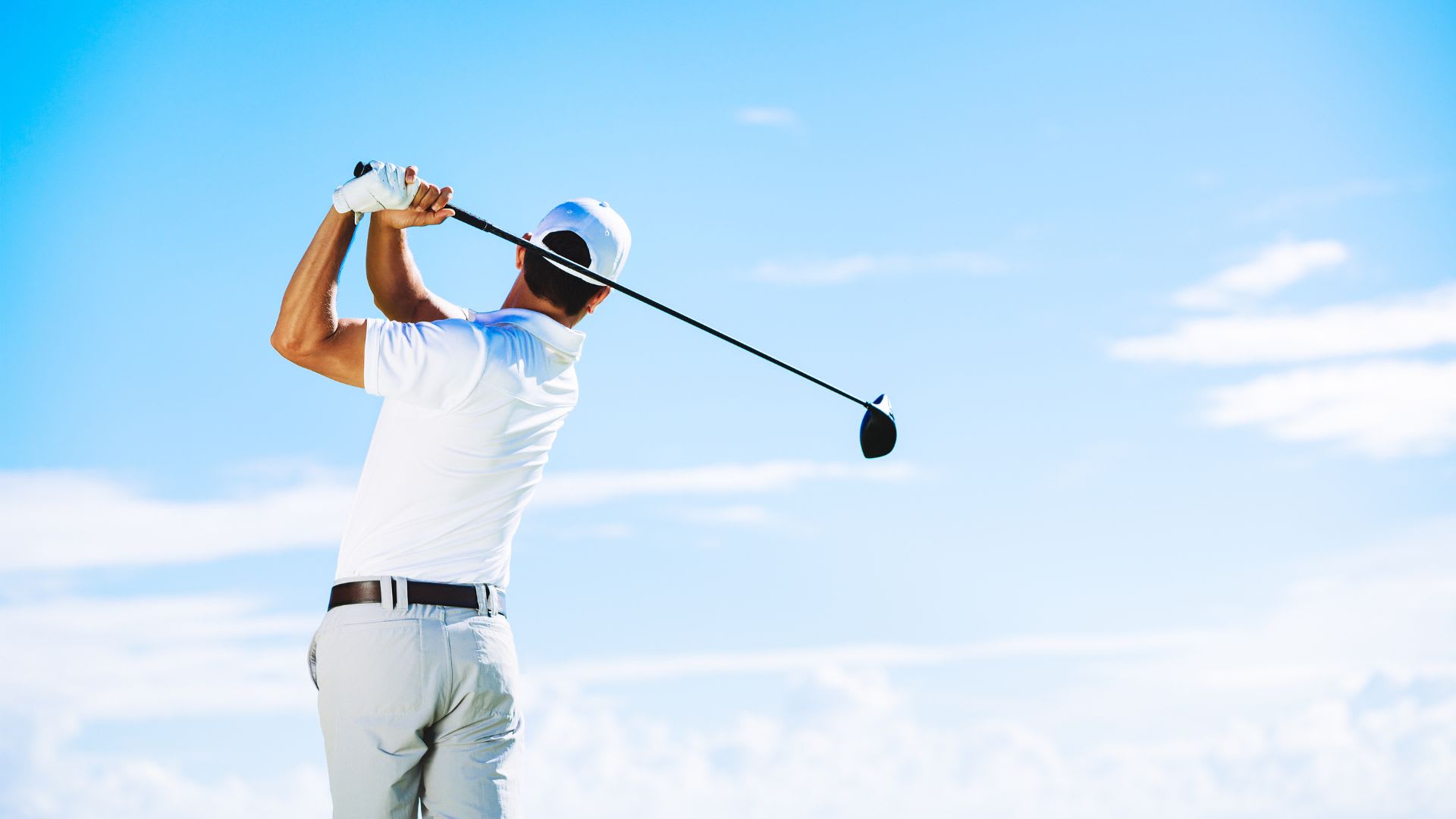 A golfer in a cap and gloves swings a club under the clear blue sky, aiming for that perfect under-par score that every enthusiast dreams of achieving.